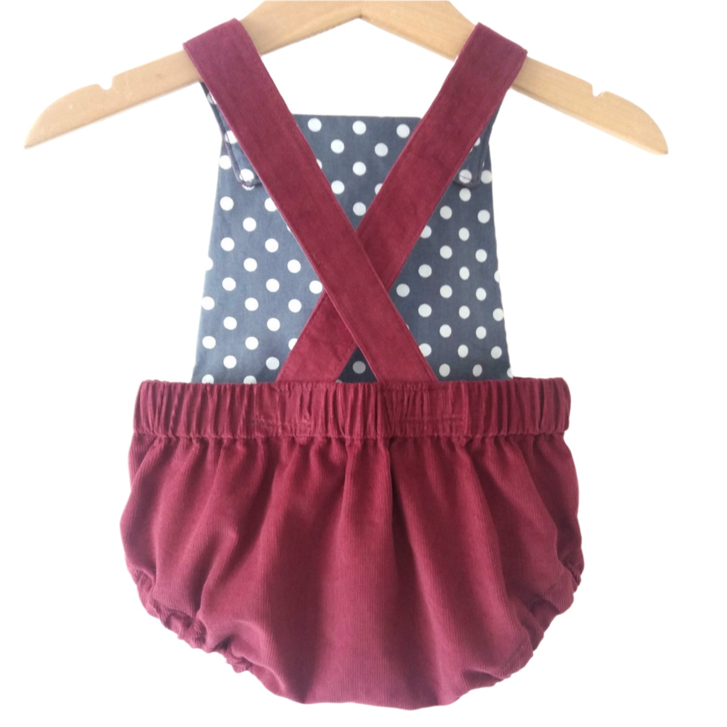 burgundy corduroy bloomer-style baby romper, with a grey polka dot lining, displayed on a hanger