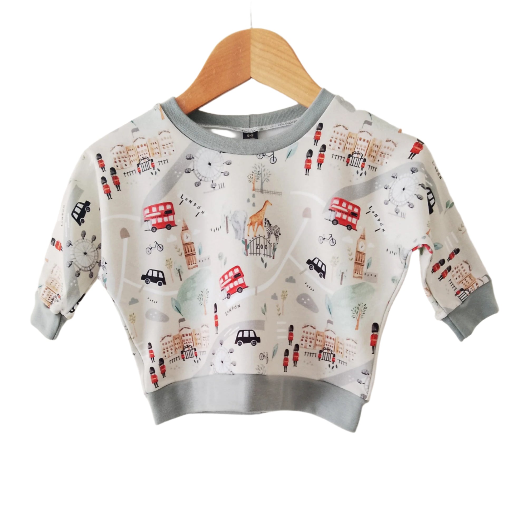 beige baby sweatshirt with illustrations of london tourist attractions, displayed on a wooden hanger