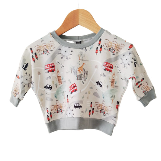 beige baby sweatshirt with illustrations of london tourist attractions, displayed on a wooden hanger