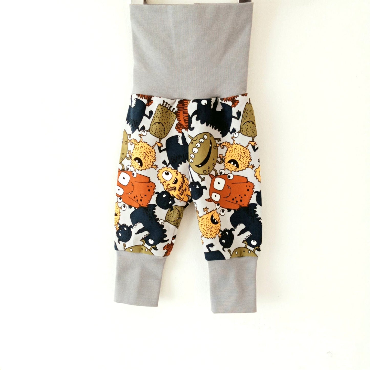 Still life of light grey Khudu Kids baby sweat pants with foldover waistband and ankle cuffs, featuring colourful cartoon monsters and aliens.